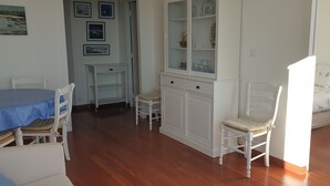 Ein Zimmer mit Esstisch, Stühlen, einer Vitrine, einem Bett und einem kleinen Tisch mit Stuhl.