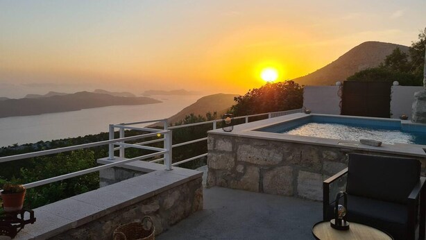 A rooftop terrace with a swimming pool, a chair, a table, and a view of the sunset over a body of water and hills. - Amber's Place, Cosy House With Pool and sea Views (Dubrovnik)