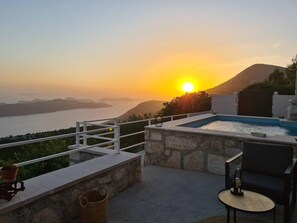 A rooftop terrace with a swimming pool, a chair, a table, and a view of the sunset over a body of water and hills. - Amber's Place, Cosy House With Pool and sea Views (Dubrovnik)