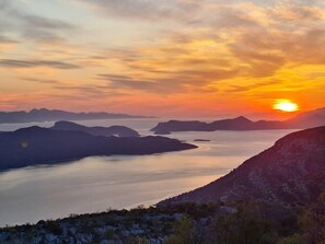 Panoramisch uitzicht op een kustlandschap met bergen en een waterlichaam tijdens zonsondergang.