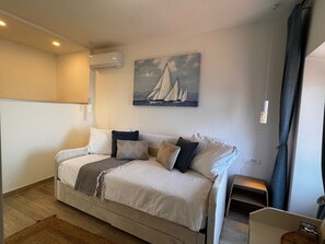 A modern bedroom with a bed, a painting of sailboats, an air conditioning unit, and a small bedside table. - Amber's Place, Cosy House With Pool and sea Views (Dubrovnik)