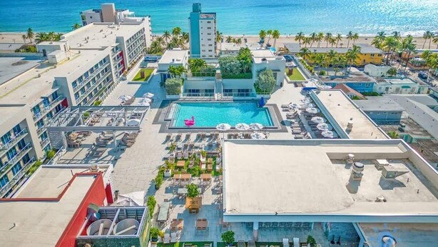 Oversigtsbillede af et hotel med swimmingpool, flere bygninger og en strand i baggrunden.