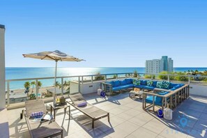 A rooftop terrace with a view of the ocean, a blue sofa, a sun lounger, and a table with a chair.