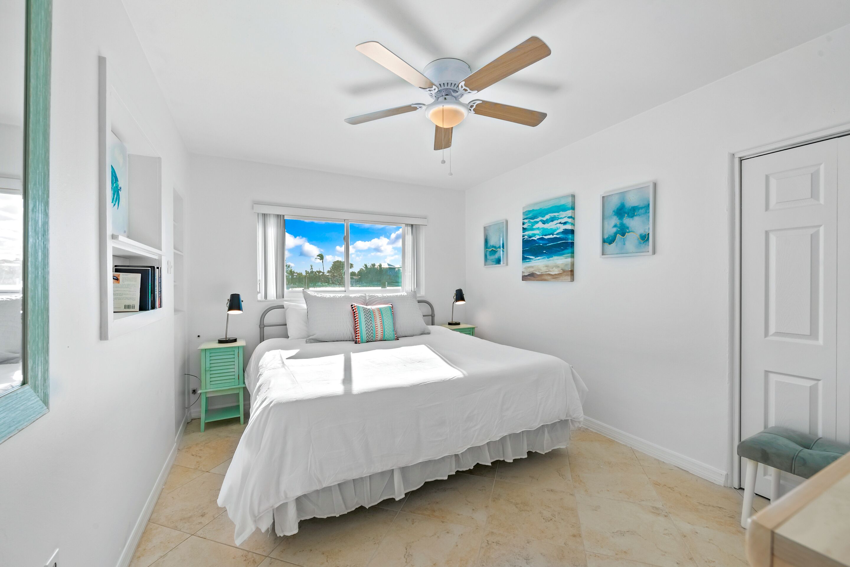 A bedroom with a bed, a ceiling fan, a window, and artwork on the walls.