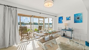 Uma área de refeições com mesa e cadeiras de madeira, um banco e vista para o mar.