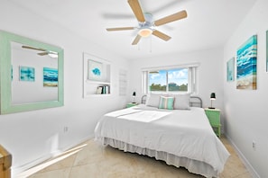 Une chambre dotée d’un grand lit, d’un ventilateur de plafond, d’une fenêtre avec vue et d’œuvres d’art accrochées aux murs.