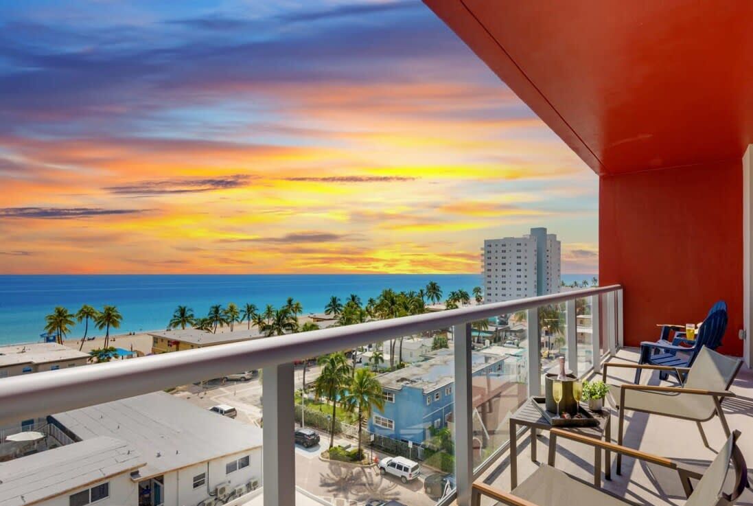 A balcony with a view of the ocean and palm trees during sunset.
