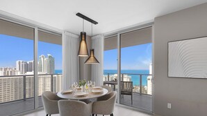 A modern dining area with a round table set for four, large windows offering a cityscape view, and a ceiling-mounted pendant light. - Wrap Around Balcony: Paradise Beach|Amazing Pools (Hollywood)