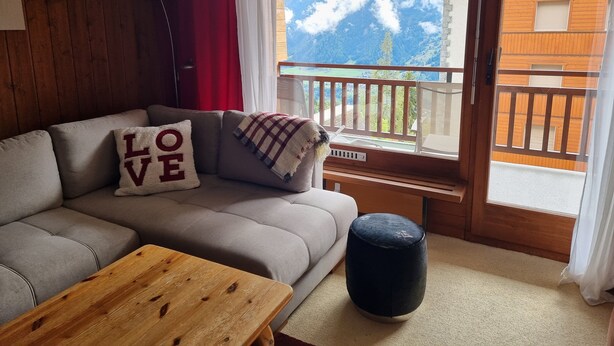 Ein gemütliches Wohnzimmer mit einer Couch, einem Couchtisch und Bergblick vom Balkon.