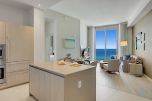 A modern living room with a large window offering a view of the sea. - Beachfront Condo | Front Oceanview Balcony+ Pools (Hollywood)