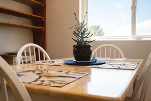 A dining table with a potted plant, white chairs, and a window with a view of trees. - Crestone Mountain Retreat House: Quiet in Nature (Saguache County)