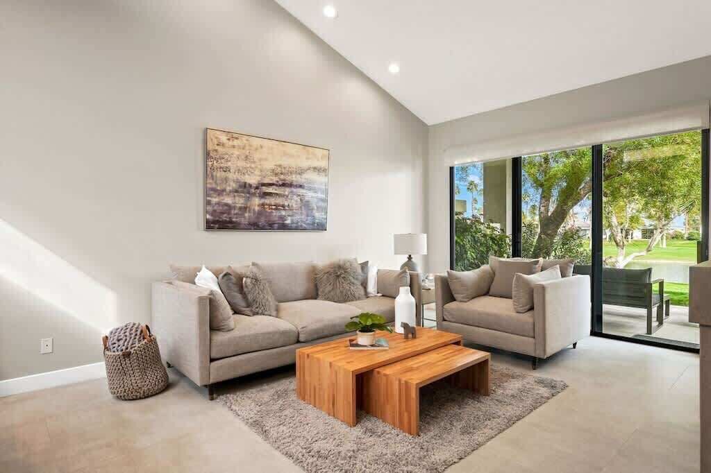 Ein modernes Wohnzimmer mit zwei Sofas, einem Couchtisch und einem großen Fenster mit Blick ins Freie.
