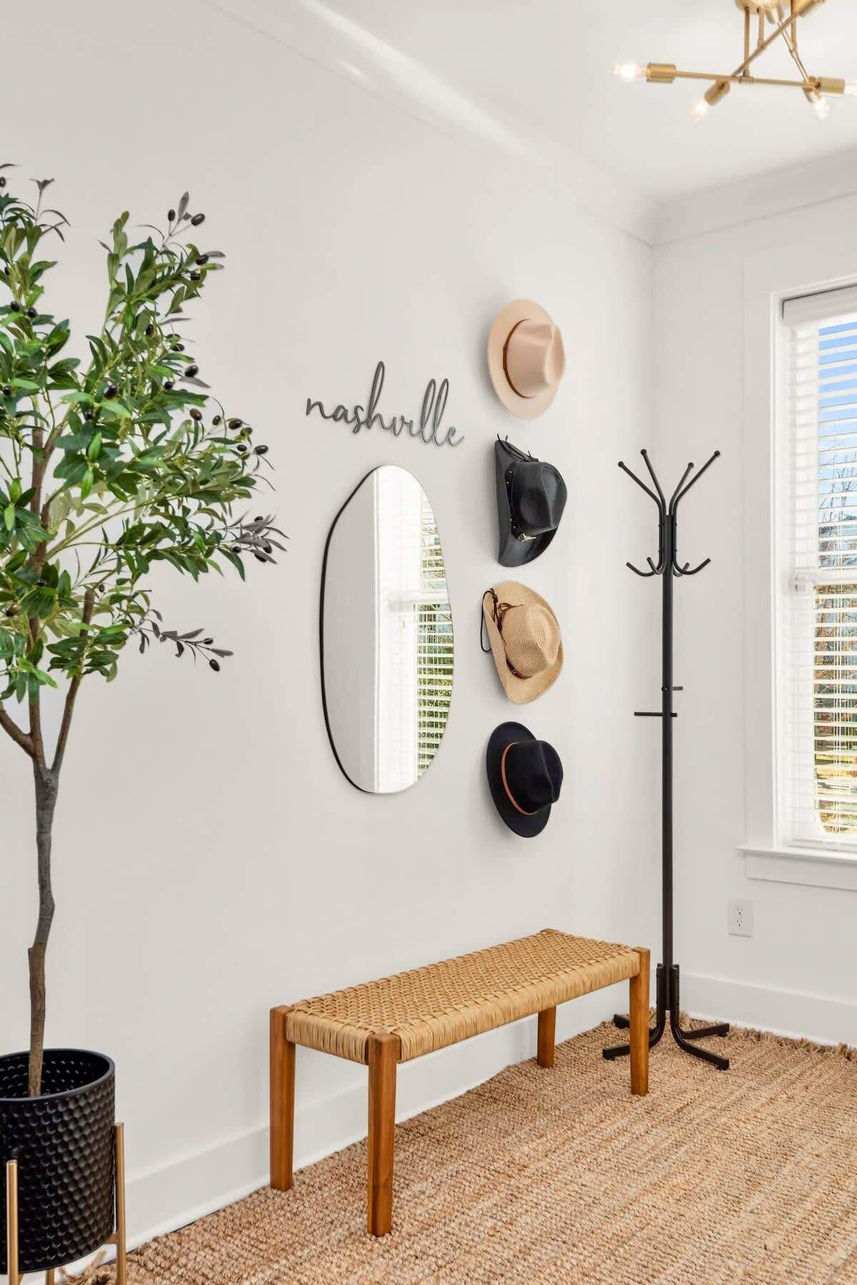 Ein Zimmer mit weißer Wand, einem Spiegel, einer Bank, einem Kleiderhaken und einem Blumentopf.