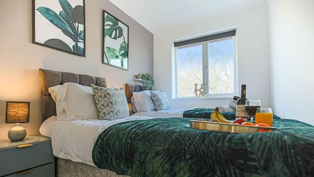 Une chambre à coucher avec un lit, une table de chevet, une fenêtre et des œuvres d’art accrochées au mur.