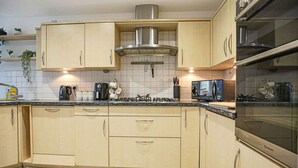 Une cuisine moderne avec des meubles en bois clair, des appareils en acier inoxydable et un dosseret carrelé.