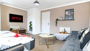 Un salon avec un baby-foot, un téléviseur affichant le logo « NETFLIX », un canapé, une table basse et une porte.