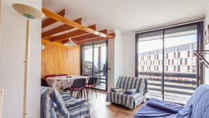 A cozy living area with a sofa, armchairs, and a dining table. There is a large window offering a view of buildings outside. - L'Altitude - Appartement avec balcon au pied des pistes (Saint Lary-Soulan)