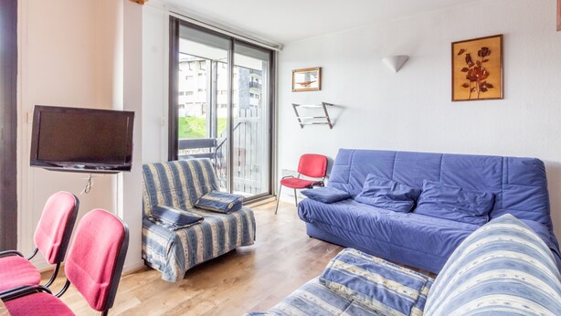 A living room with a blue sofa, striped armchair, and red chairs. A flat-screen TV is mounted on the wall. - L'Altitude - Appartement avec balcon au pied des pistes (Saint Lary-Soulan)