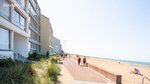 A coastal walkway with buildings on one side and a beach on the other. - La Plage - Appartement vue mer (Courseulles-sur-Mer)