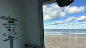 A view of the beach from inside a room with a signboard displaying various destinations. - La Plage - Appartement vue mer (Courseulles-sur-Mer)