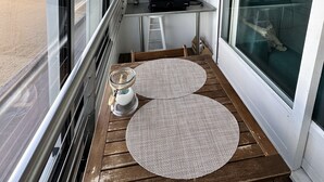 A balcony with a view of the beach, a small kitchen area with a table and stools, and a hanging light fixture. - La Plage - Appartement vue mer (Courseulles-sur-Mer)