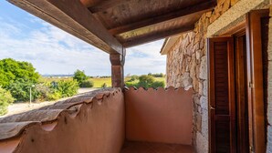A balcony with a stone wall, wooden ceiling, and a view of greenery and hills. - Appartamenti Pedra Rosa (San Teodoro)