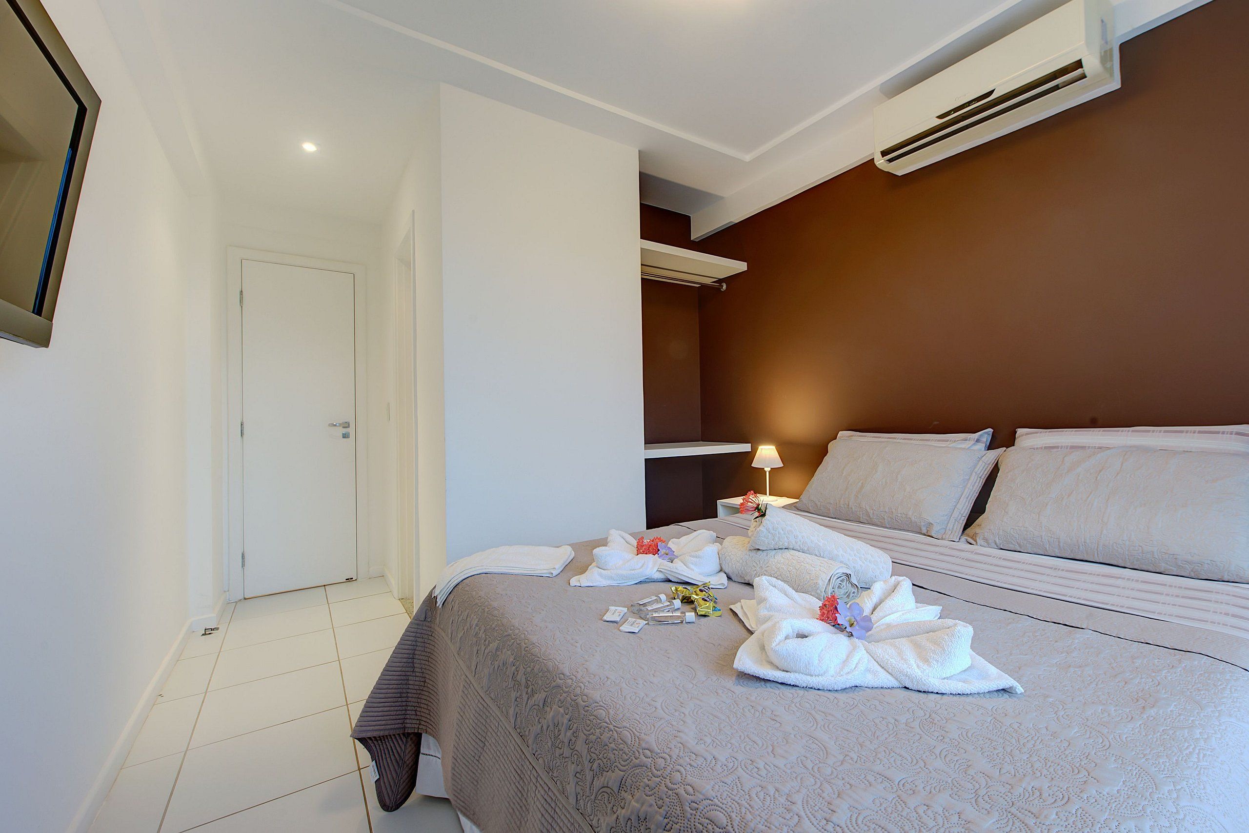 Una habitación de hotel con una cama bien hecha, una mesita de noche con lámpara y un aire acondicionado instalado en la pared.
