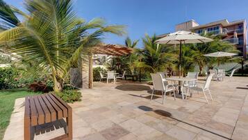 An outdoor patio with stone flooring, white metal chairs, and umbrellas.
