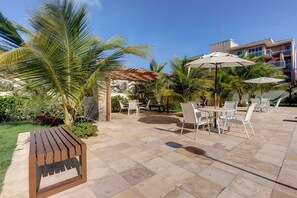 An outdoor patio with stone flooring, white metal chairs, and umbrellas.