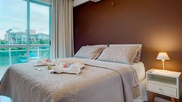 Habitación de hotel con una cama grande, una mesita de noche, una lámpara y vistas a edificios a través del ventanal.