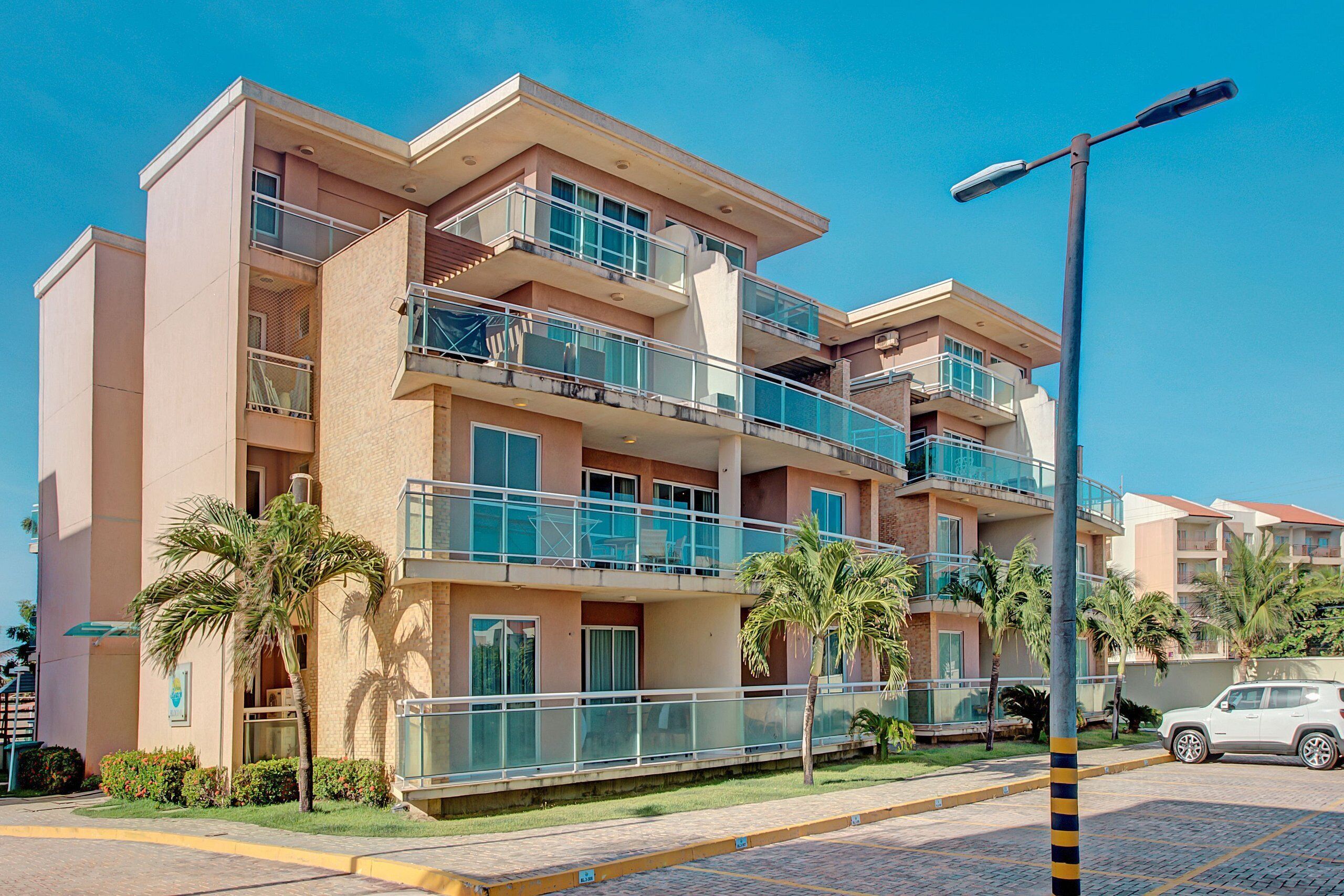 Un hotel de varios pisos con balcones, palmeras y una calle pavimentada.