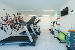 Een sportschool met loopbanden, fitnessballen en een muurschildering van atleten.