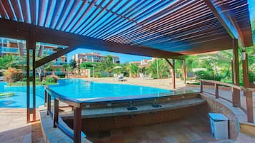 Un área de piscina con zona de estar cubierta y vistas de edificios circundantes.