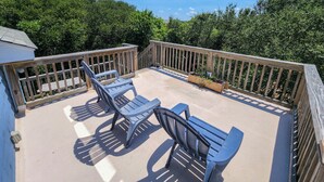Une terrasse couverte avec une plateforme en bois, deux chaises bleues et une table.
