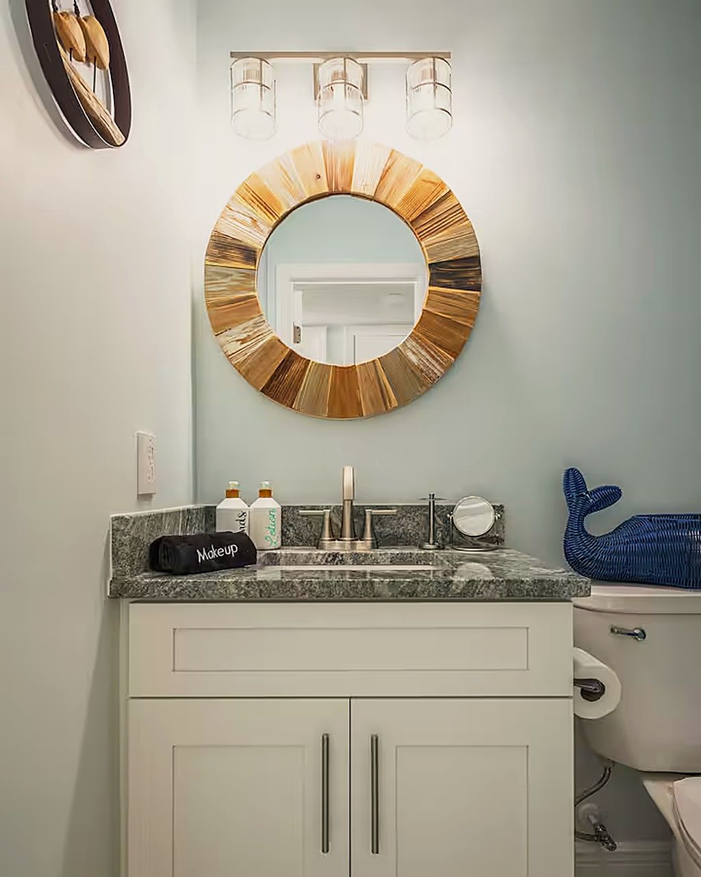 A bathroom with a round mirror, a sink with a marble countertop, and a toilet.