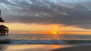 A beach with a wooden structure extending into the water, waves crashing onto the shore, and a sunset in the background. - FamilyRetreat~SeminoleTikiHut~MiniGolf~Walk2Beach~HeatedPool~FirePit~BeachGear (Cocoa Beach)