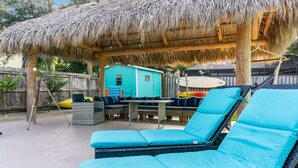 A covered outdoor seating area with lounge chairs and a thatched roof. - FamilyRetreat~SeminoleTikiHut~MiniGolf~Walk2Beach~HeatedPool~FirePit~BeachGear (Cocoa Beach)
