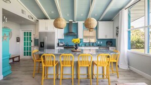 A kitchen with a central island, yellow chairs, and a large window. - FamilyRetreat~SeminoleTikiHut~MiniGolf~Walk2Beach~HeatedPool~FirePit~BeachGear (Cocoa Beach)