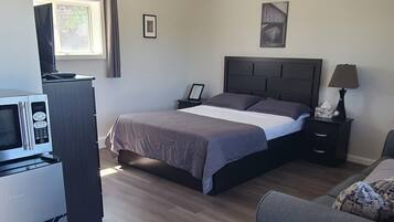 Un dormitorio con cama, mesita de noche, lámpara y escritorio con computadora y microondas.
