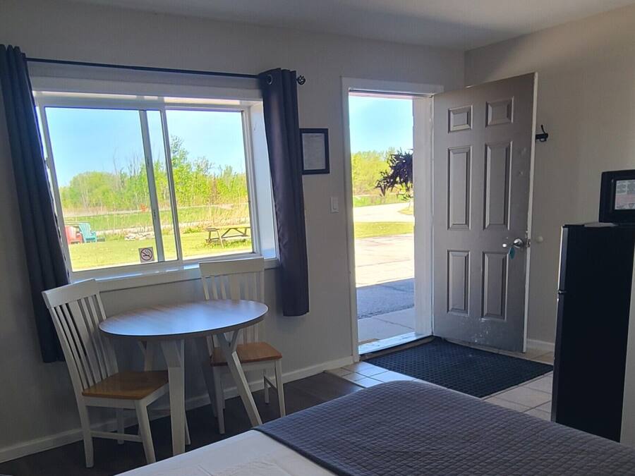 A hotel room with two beds, a dining table, chairs, a refrigerator, and a view of the outdoors.