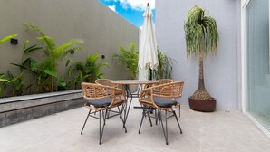 Un patio con sillas de mimbre, una mesa redonda y una planta en maceta.