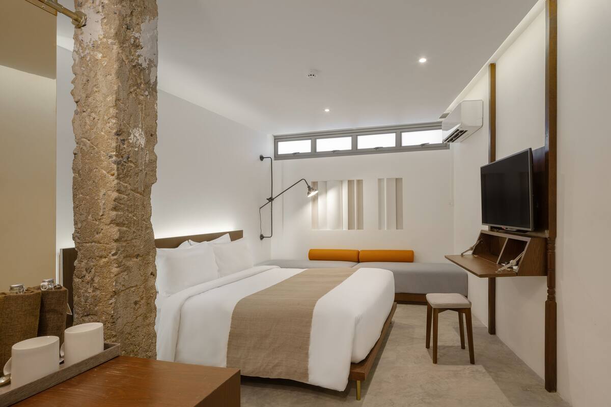 A modern hotel room with a large bed, a desk, a television, and a stone accent wall.