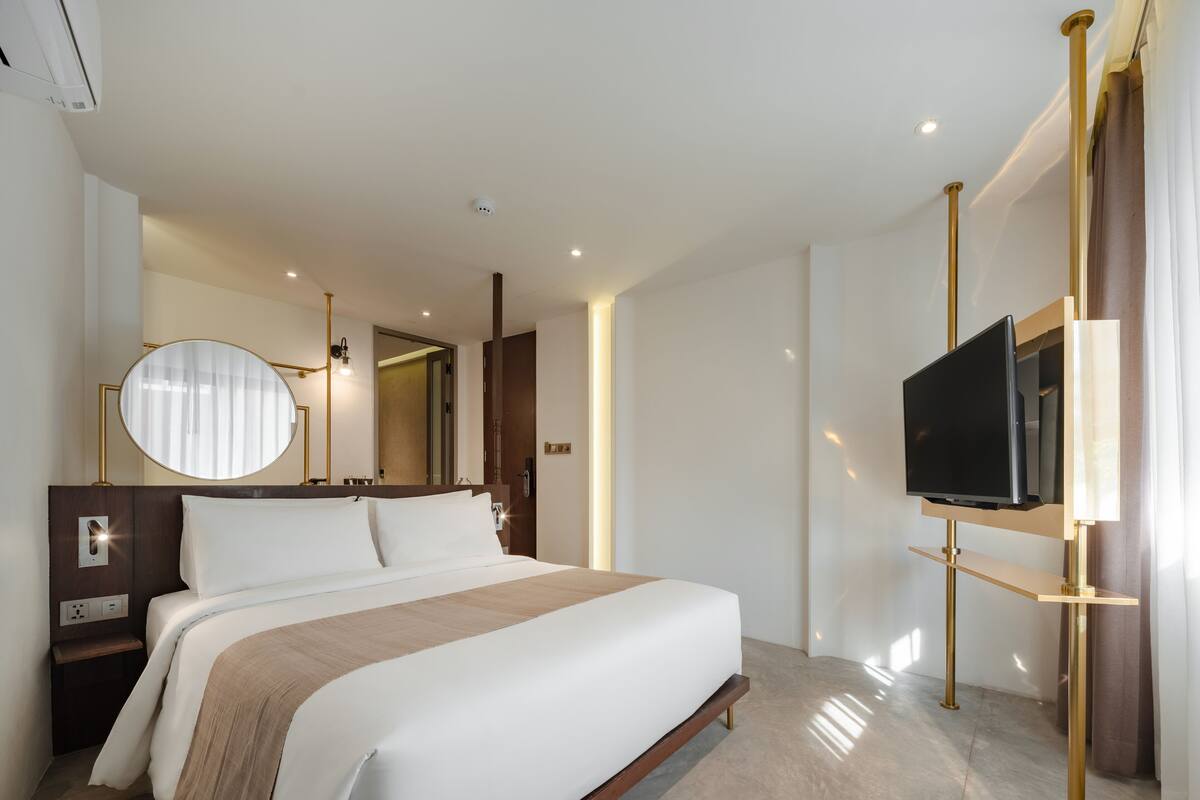 A modern hotel room with a large bed, a TV mounted on the wall, a bedside table, and a mirror.