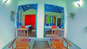 A room with two wooden chairs and a small table, a bed with red curtains, and a view through an open doorway. - Charming Villa With Pool, Near Beach, Sri Lanka (Kahandamodara)