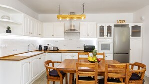 Una cocina moderna con armarios blancos, una mesa de comedor de madera y un refrigerador de acero inoxidable.