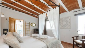 Un dormitorio con cama, una silla, una escalera, un espejo y un elemento decorativo en la pared.