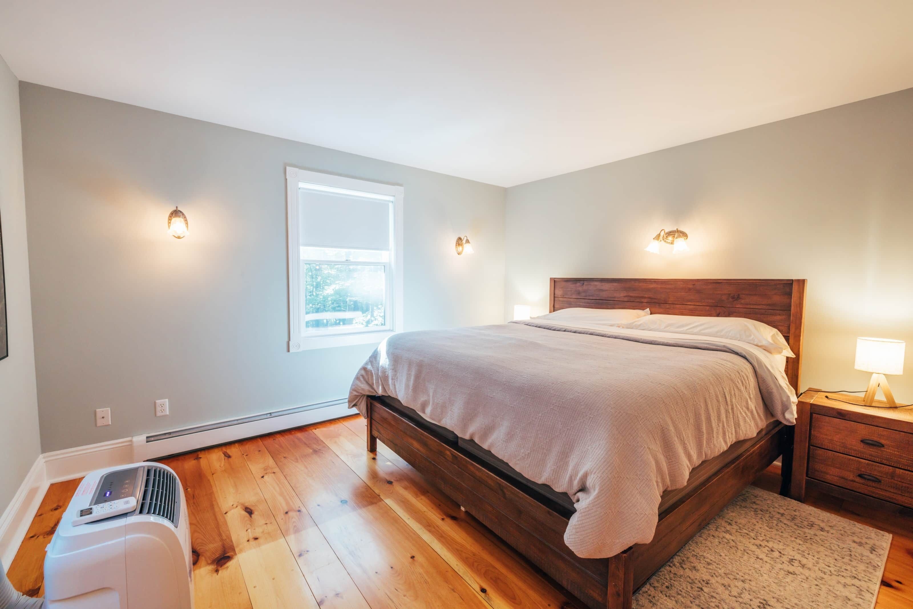 A bedroom with a wooden bed, a heater, a window, and wall-mounted lights.