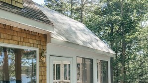 Une terrasse couverte avec une table et des chaises, une clôture en bois et une vue sur les arbres.