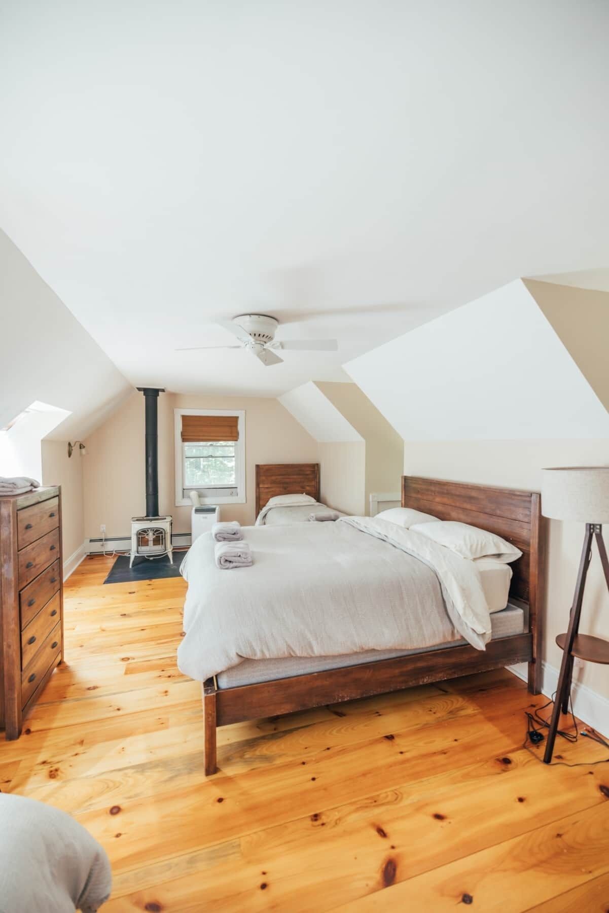 Un dormitorio con techo inclinado, una cama de madera, un aparador y un radiador.