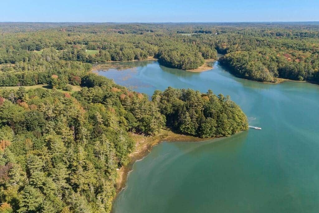 Luchtbeeld van een meer, omringd door dicht bos, met een klein eiland en een boot.